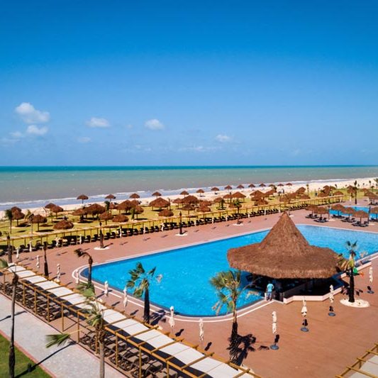 Vista aérea lateral piscina com estrutura com gazebos e cadeiras na ala praia, tudo para atender sua família