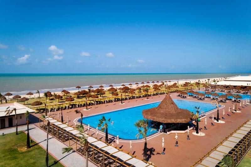 Vista aérea lateral piscina com estrutura com gazebos e cadeiras na ala praia, tudo para atender sua família